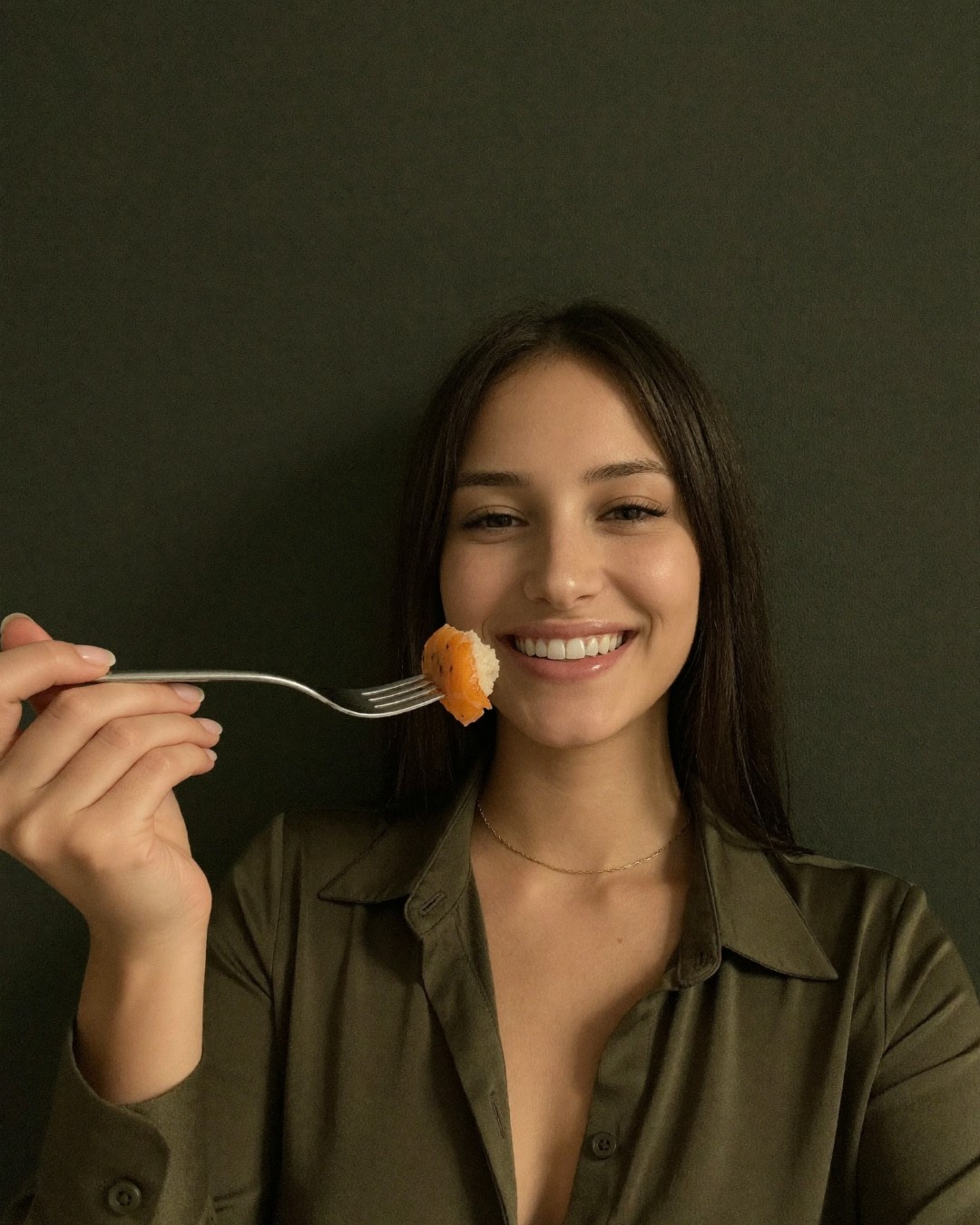 A woman holding up one bite of glazed salmon on a fork